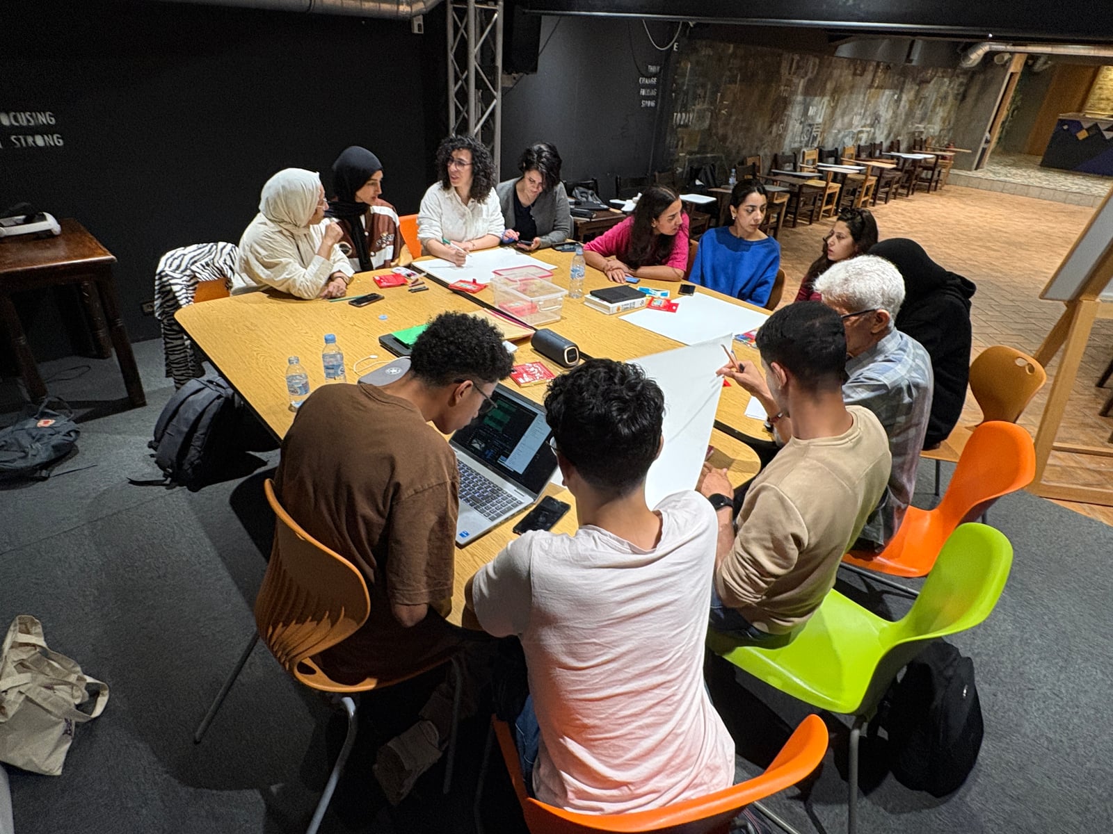 Adult workshop participants developing ideas together around a table with drawing materials and digital tools